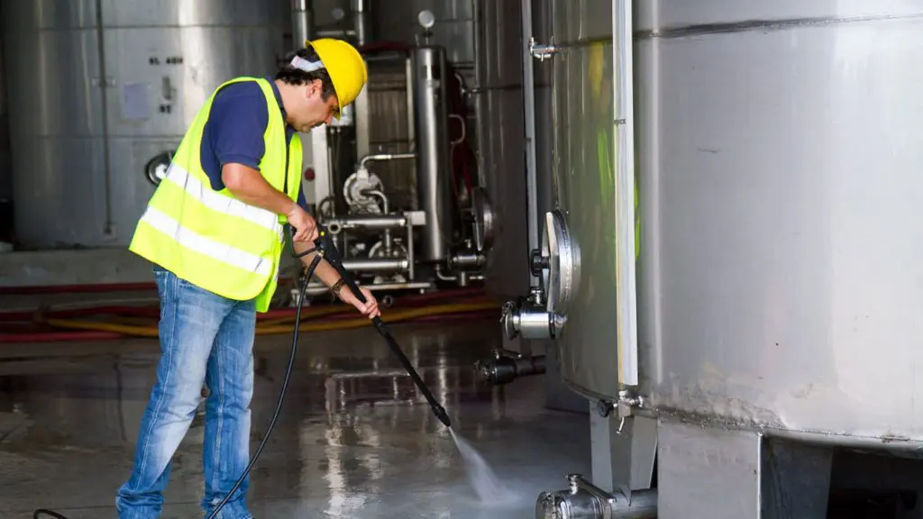 Un hombre en un chaleco amarillo se dedica a la limpieza industrial de un tanque, garantizando su funcionamiento óptimo.