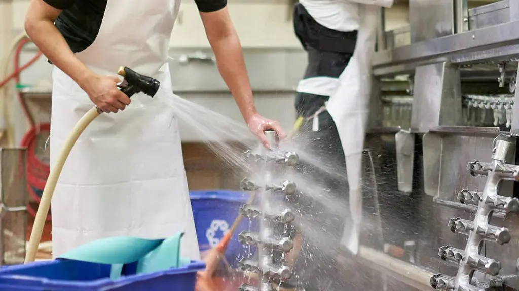 Un hombre con un delantal blanco realiza la limpieza de un equipo industrial.