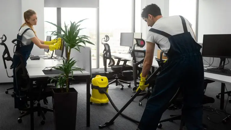 Limpieza de Oficinas – Servicio La imagen muestra a dos personas de servicio de limpieza limpiando una oficina, aspirando y limpiando pantallas