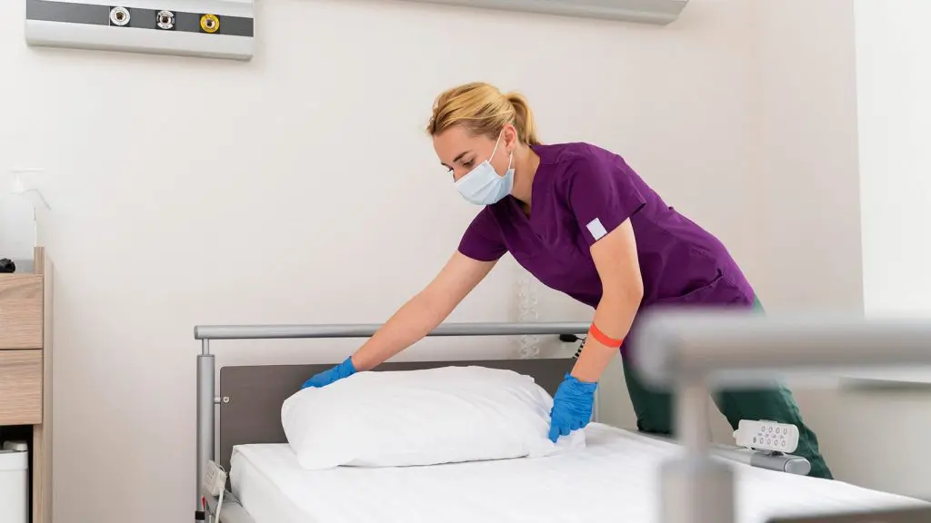 Profesional de limpieza en una sala de hospital, realizando la limpieza de una cama.