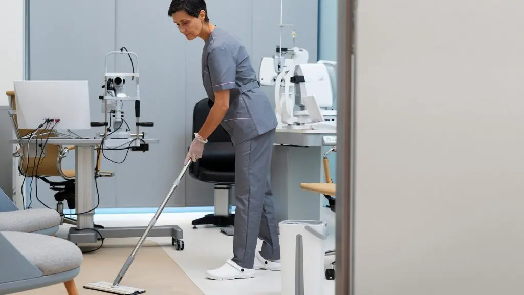 Mujer limpiando una habitación de hospital con una aspiradora, enfocándose en mantener el espacio limpio y libre de polvo.