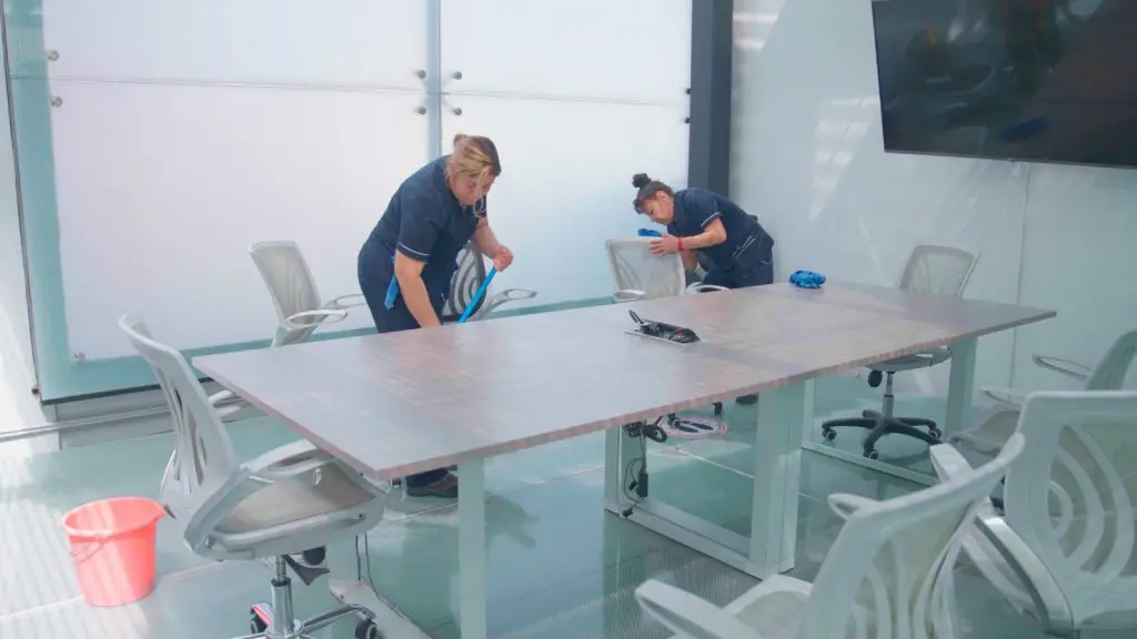 Limpieza de Oficinas – Servicio Dos mujeres organizando y limpiando una mesa de conferencias en una oficina, contribuyendo a un espacio de trabajo eficiente.