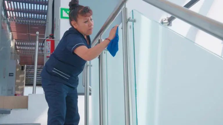 Una mujer se dedica a limpiar las barandillas de vidrio en una escalera de oficina, manteniendo la misma limpia e higiénica.