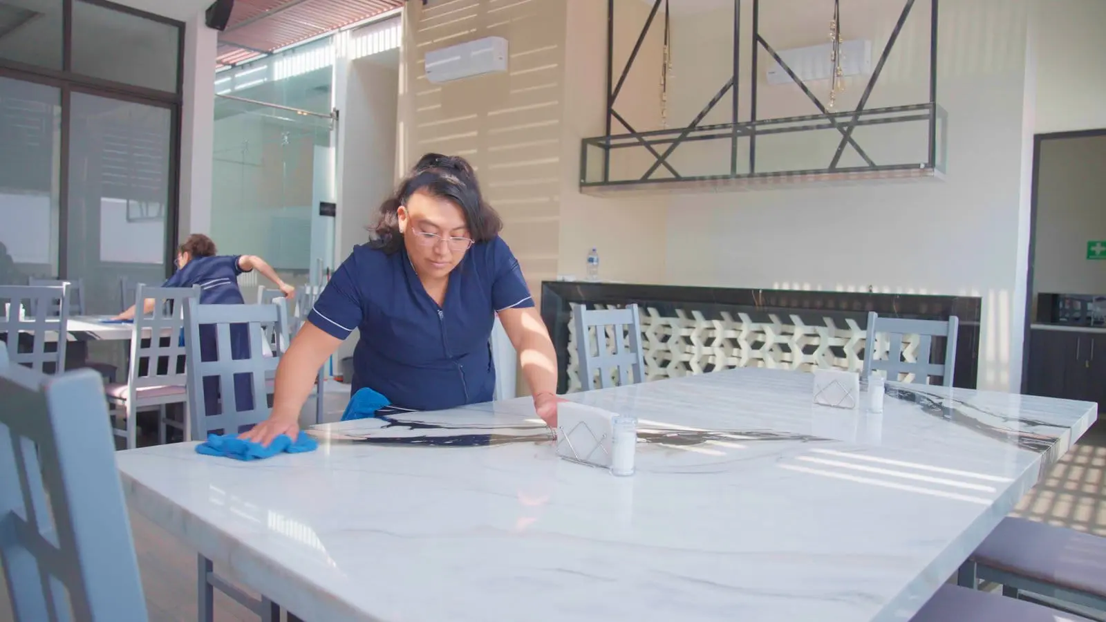 En una oficina, una mujer realiza la limpieza de una mesa del área común, contribuyendo a la presentación del lugar para los clientes.